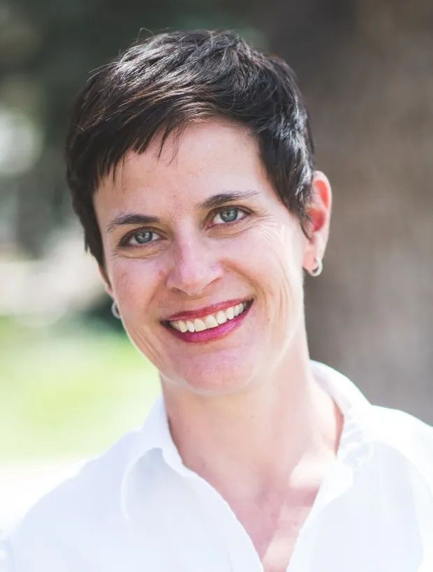 Person wearing a white shirt with short, dark brown hair and a small earring.