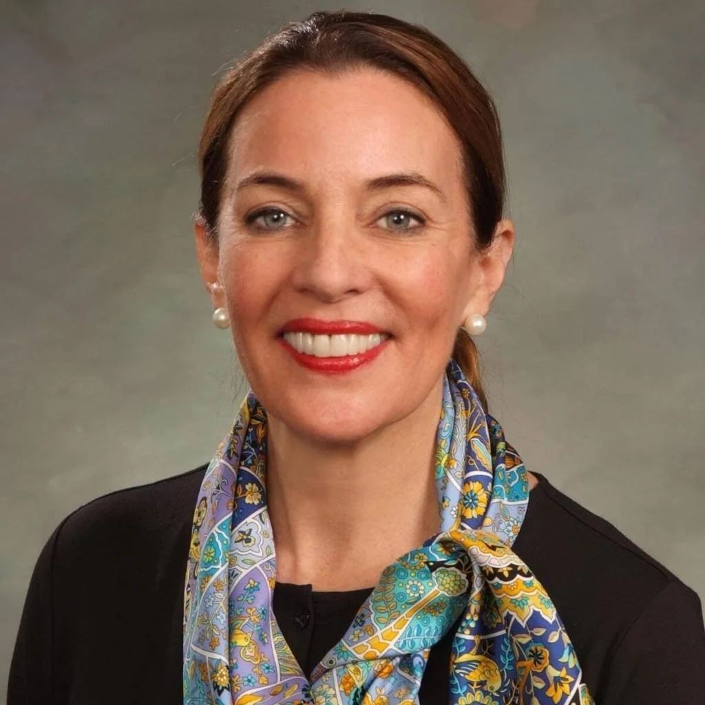 Person wearing a colorful patterned scarf over a black top, with pearl earrings against a neutral background.